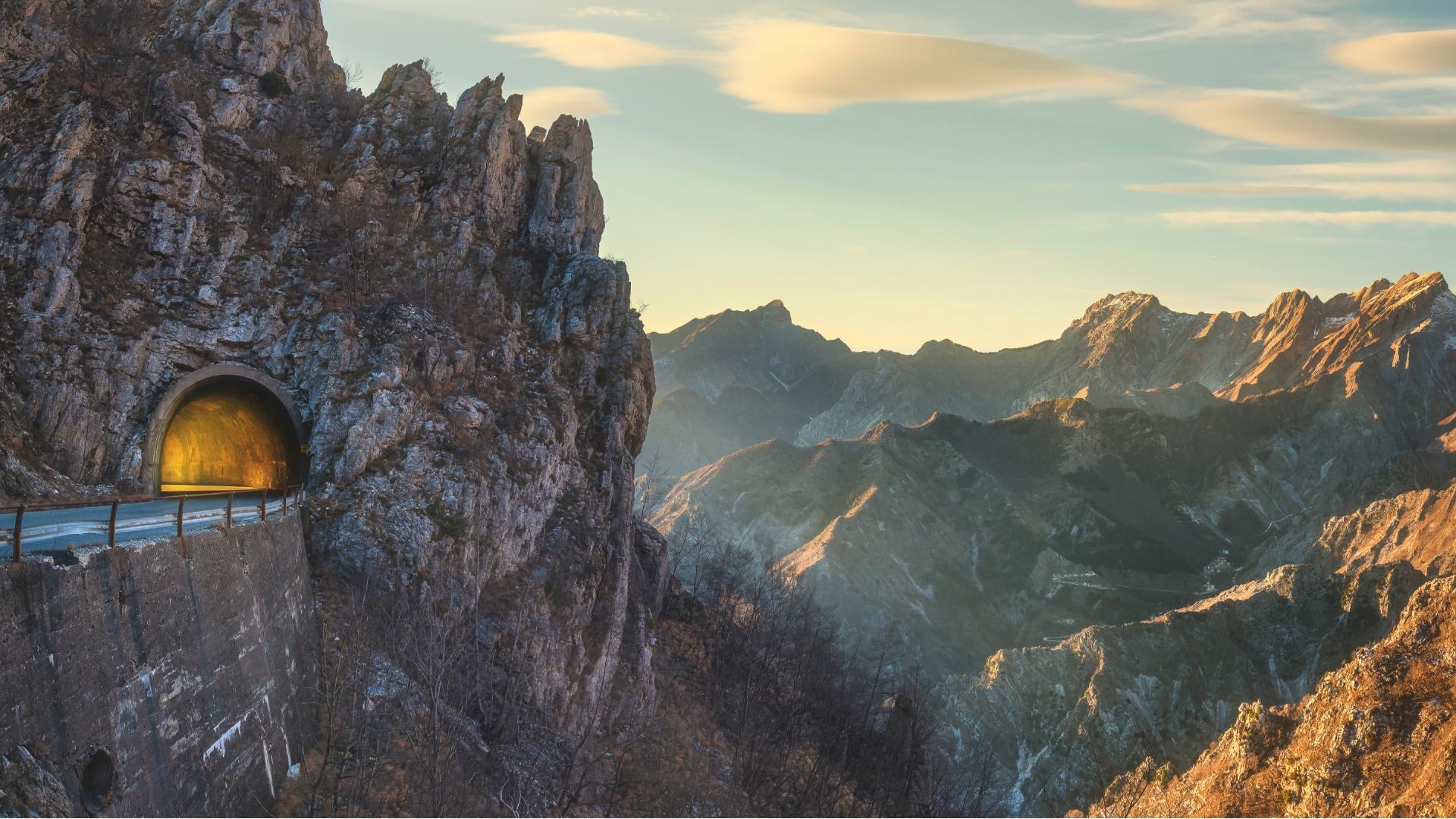 Tunnel illuminato tra montagne rocciose al tramonto, atmosfera di avventura e meraviglia.