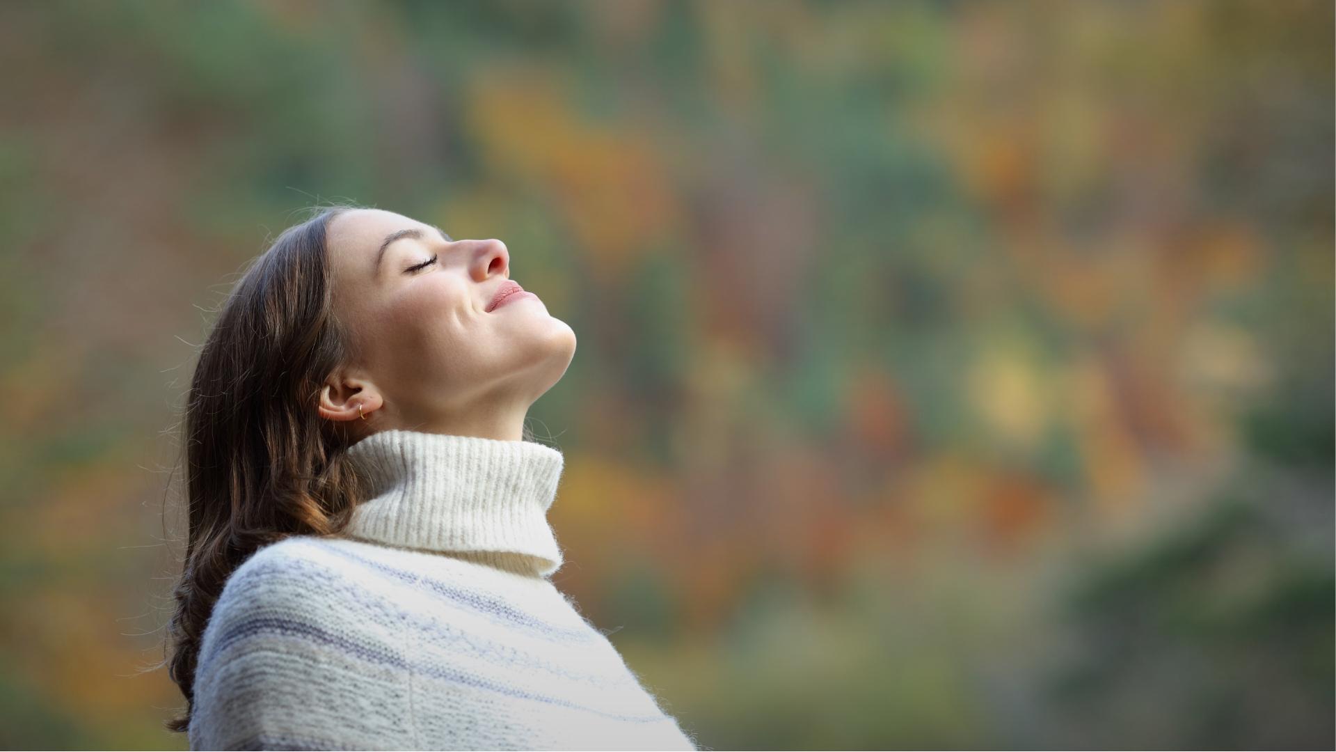 Donna felice respira profondamente all'aperto, sfondo autunnale sfocato.