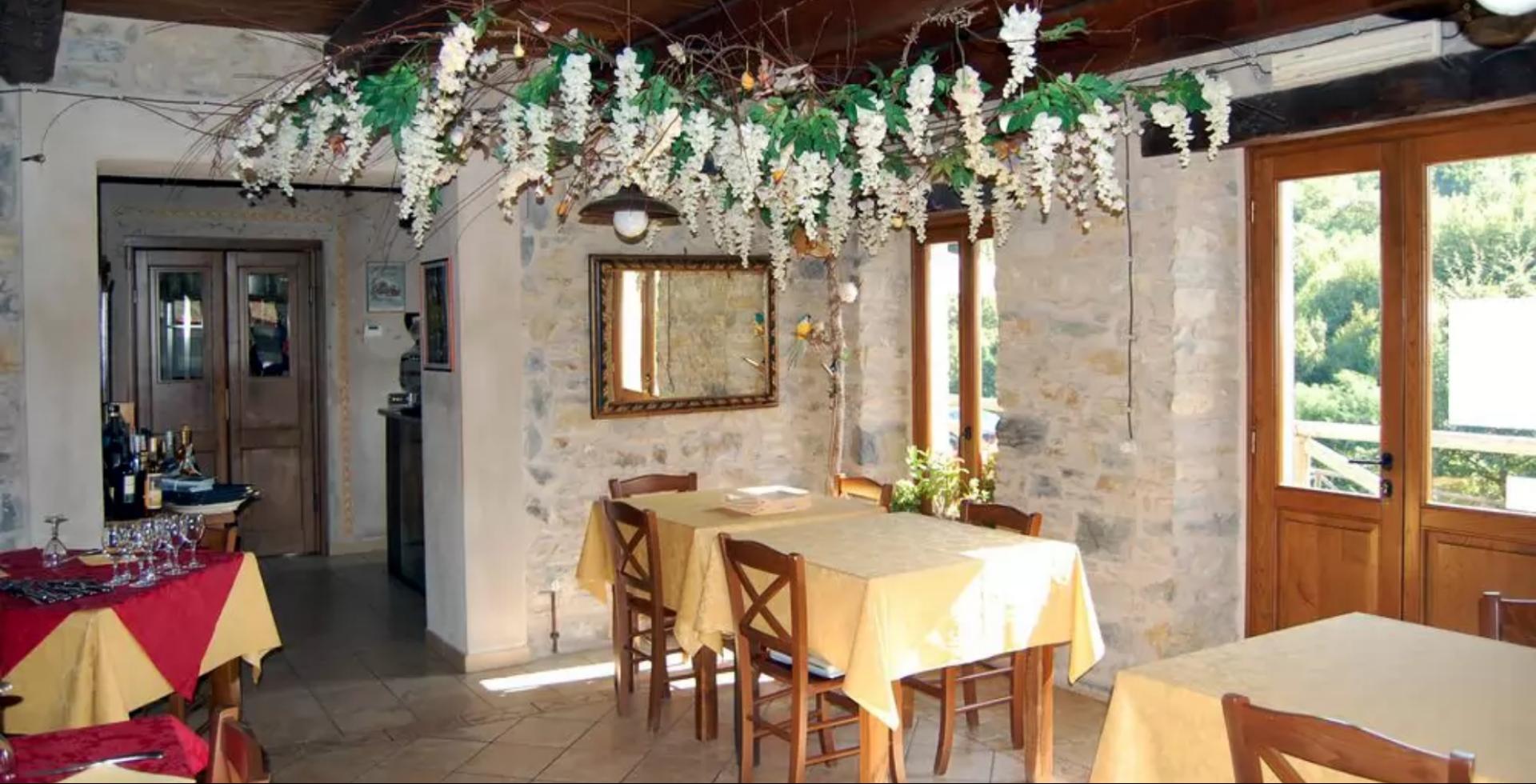 Ristorante rustico con tavoli apparecchiati, decorazioni floreali e pareti in pietra.