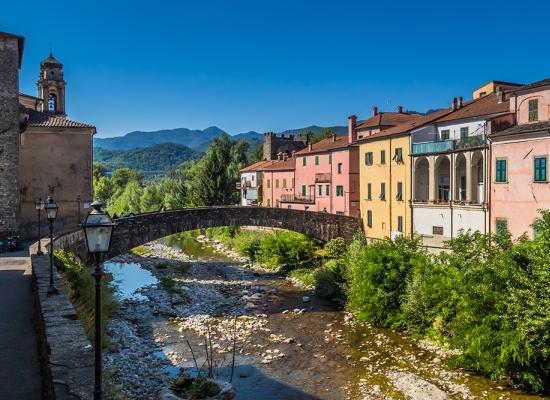 Ponte antico e case colorate lungo un fiume in un paesaggio montano.