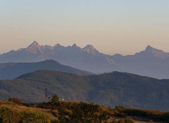 Panorama montano con colline boscose e vette illuminate dalla luce del tramonto.