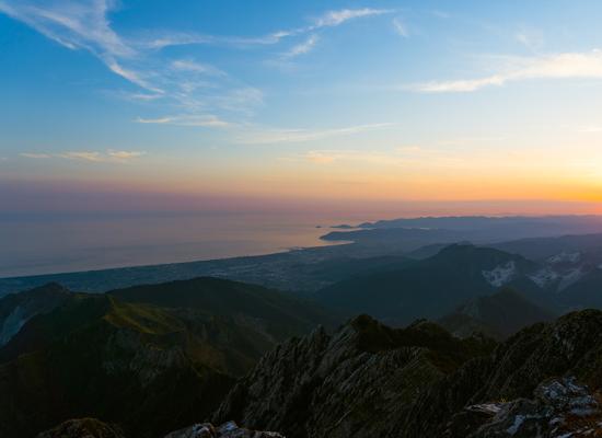 Tramonto sulle montagne con vista sul mare e paesaggio costiero.