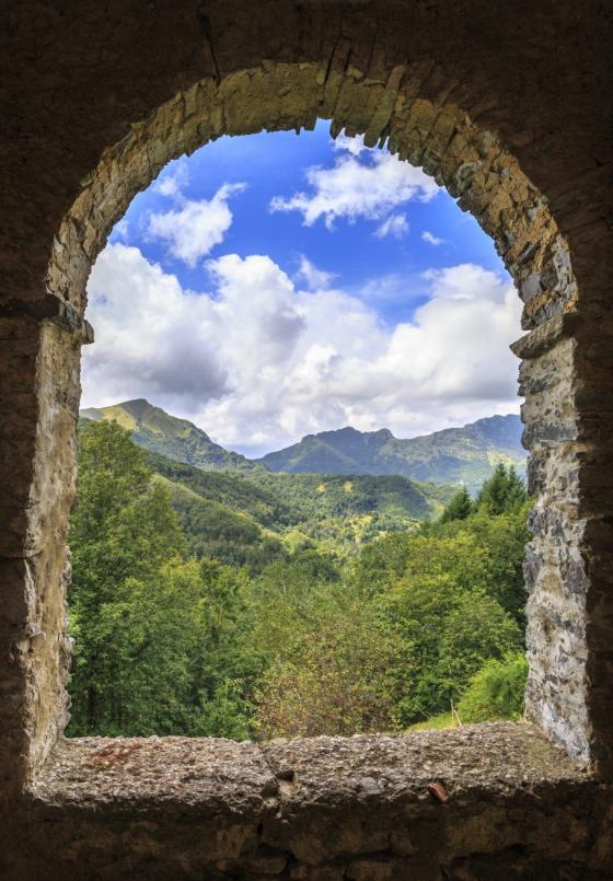 Vista di montagne e foresta attraverso un'antica finestra ad arco in pietra.