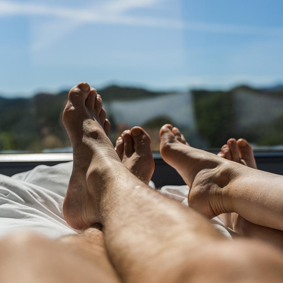 Due persone rilassate a letto, con vista su cielo e montagne.