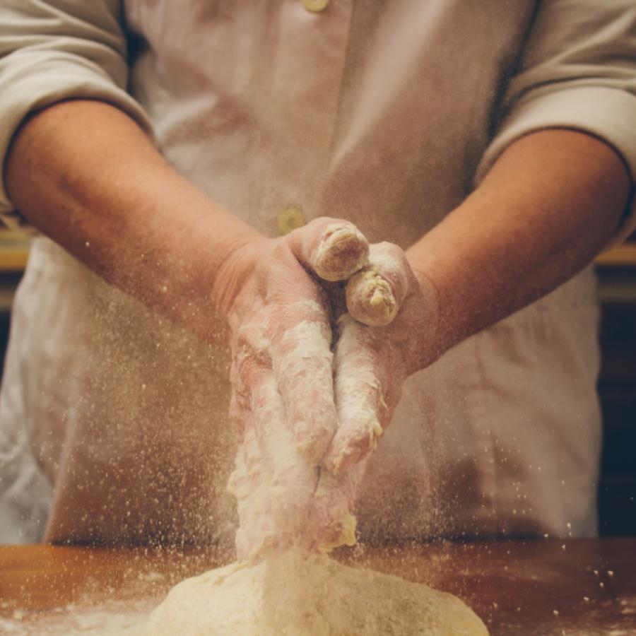 Mani che impastano farina su un tavolo di legno in cucina.